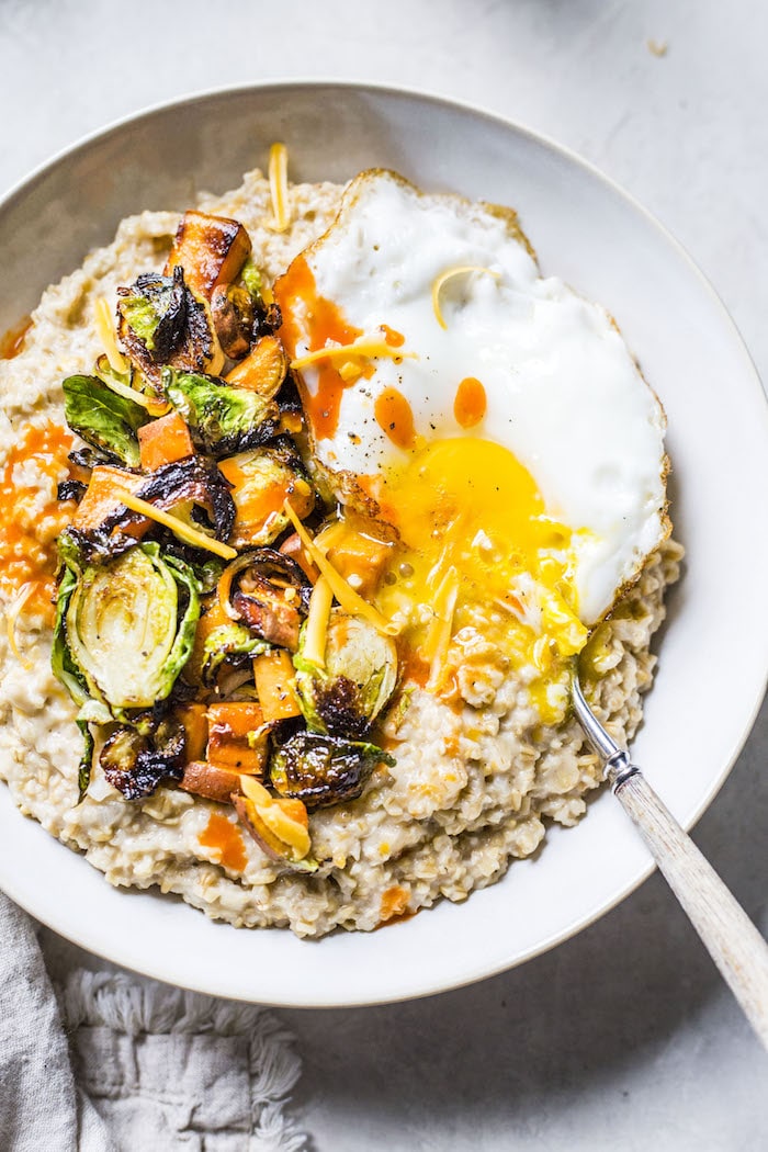 a bowl of oatmeal topped with brussels sprouts, sweet potato and a fried egg