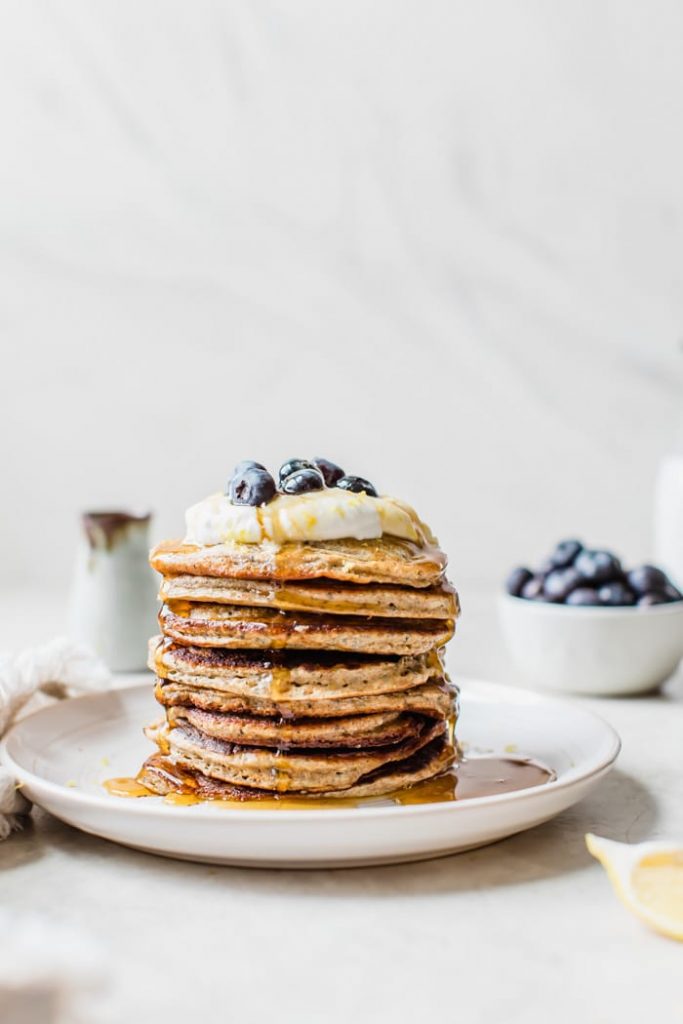 A stack of pancakes topped with Greek yogurt, lemon zest, blueberries, and maple syrup