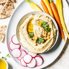 A bowl of hummus topped with chickpeas surrounded by vegetables and pita bread.