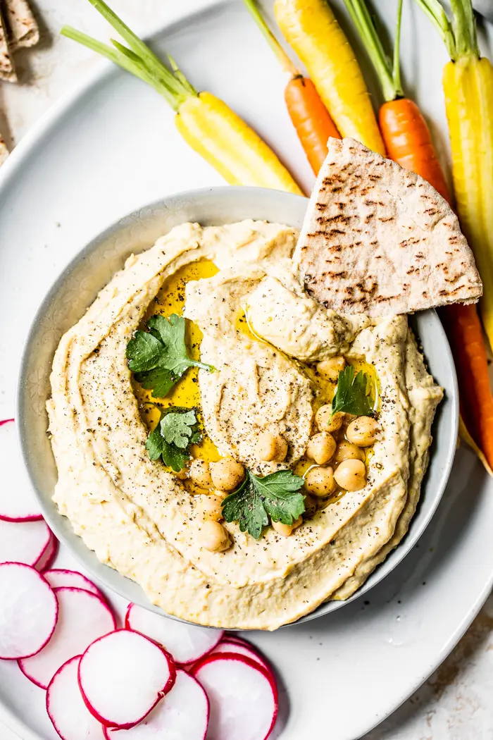 A bowl of hummus topped with chickpeas, olive oil and parsley served with pita bread and vegetables