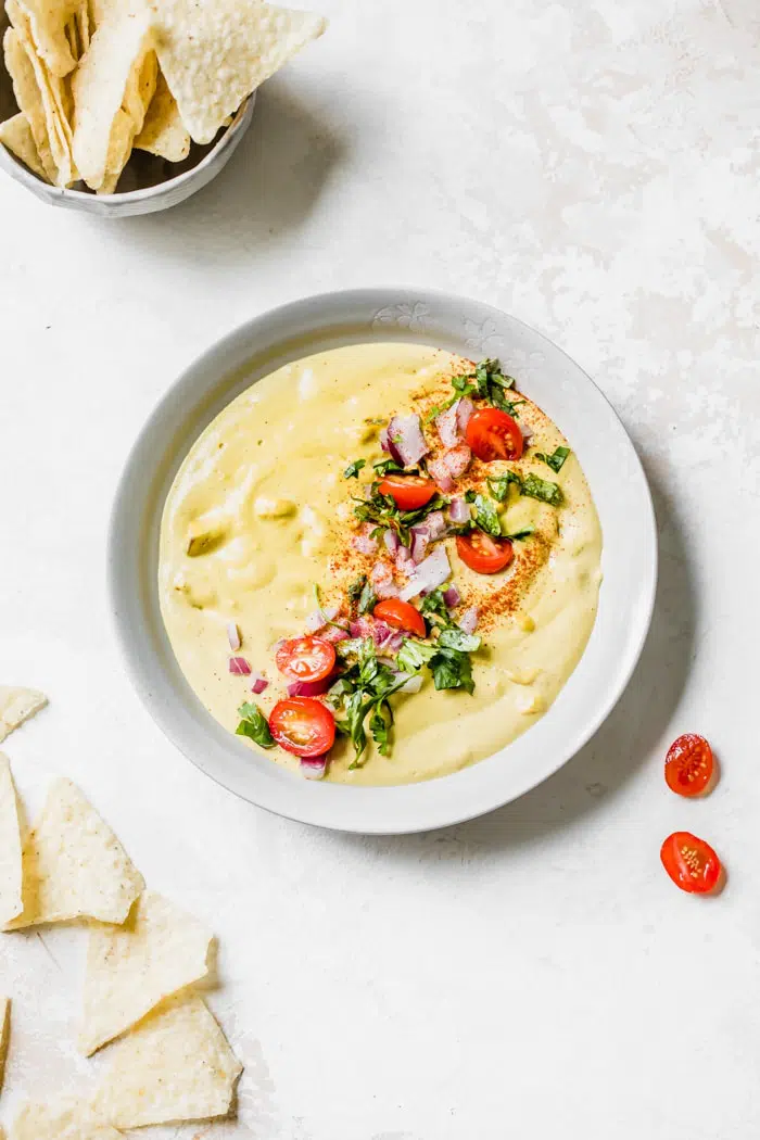 A bowl of queso topped with tomatoes, cilantro and onion