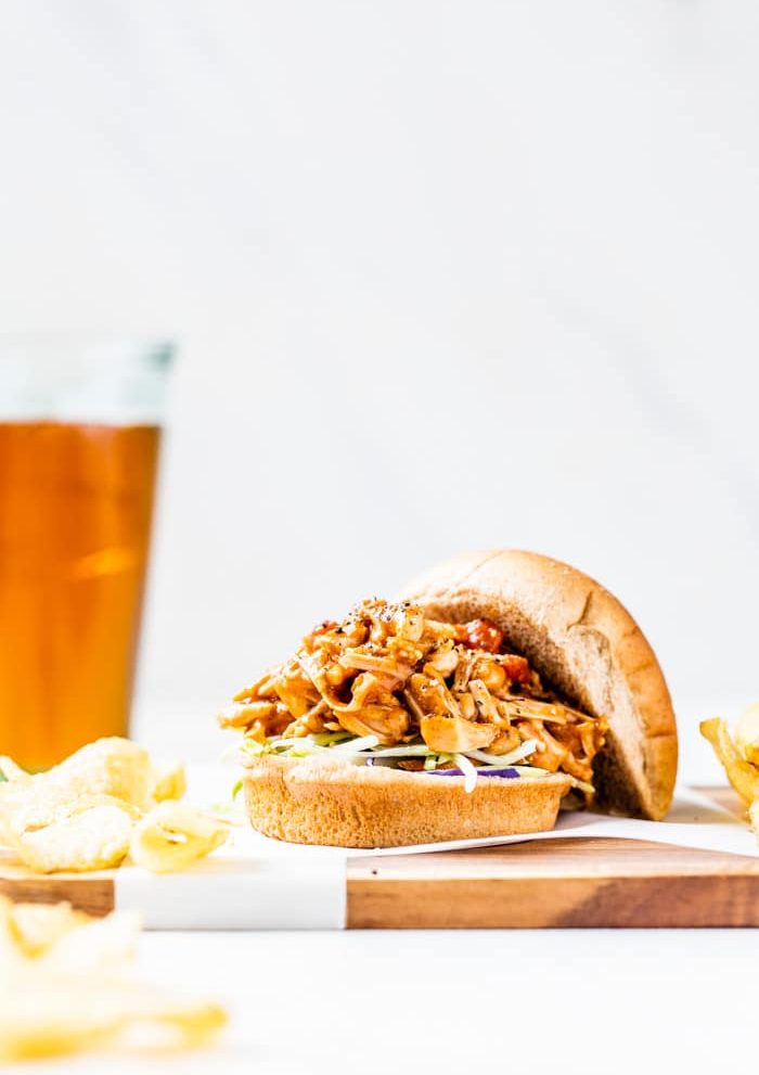 A hamburger bun filled with pulled jackfruit served with chips and beer