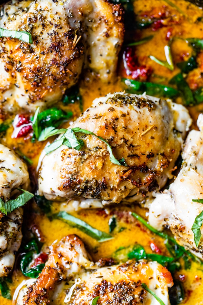 close up shot of chicken thighs covered in Italian seasoning, sun-dried tomatoes and fresh basil