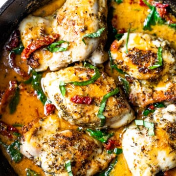Chicken thighs covered in sun-dried tomato sauce and fresh basil