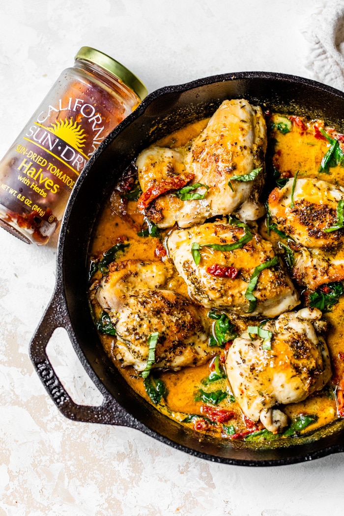 Skillet with 5 chicken thighs covered in sun-dried tomatoes and fresh basil