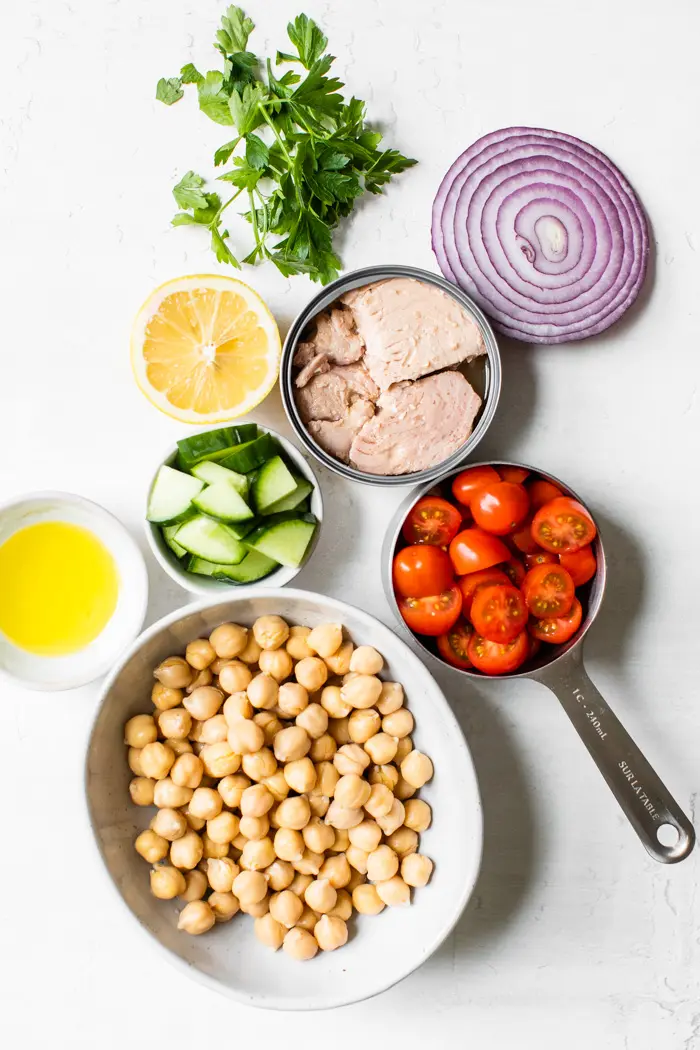 tuna, chickpeas, tomato, onion, cucumber, lemon, and parsley on a table