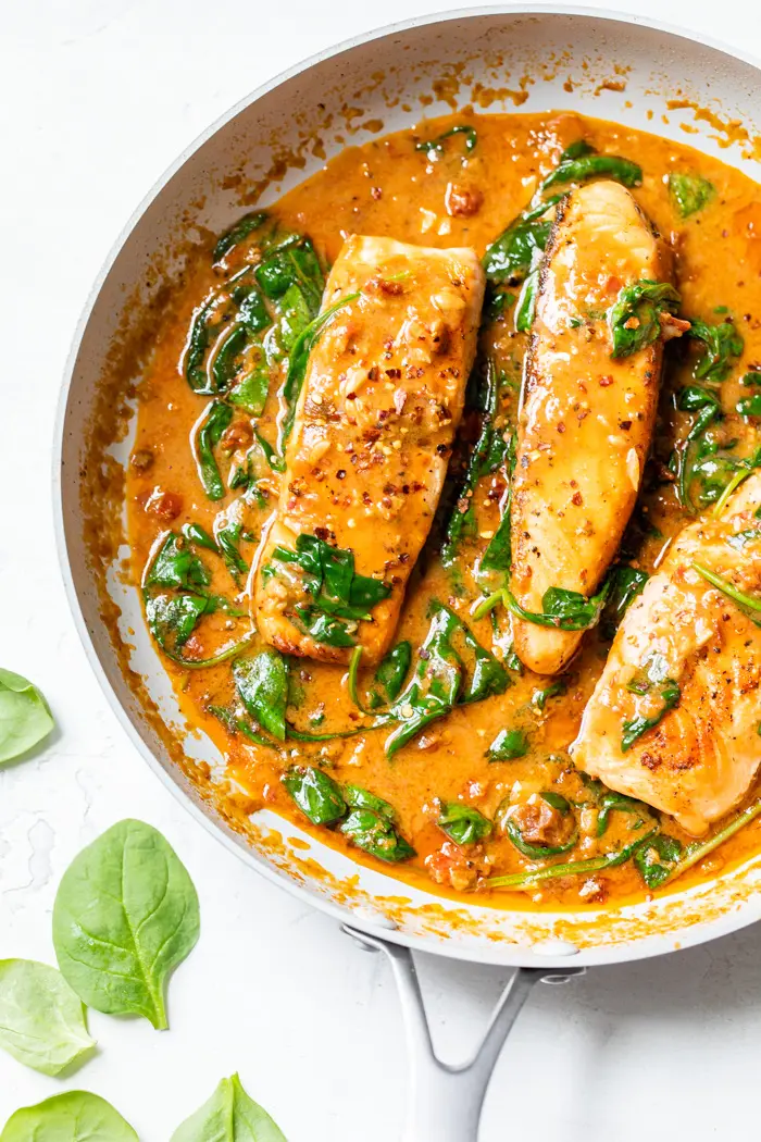 salmon in a skillet with tomato sauce and spinach