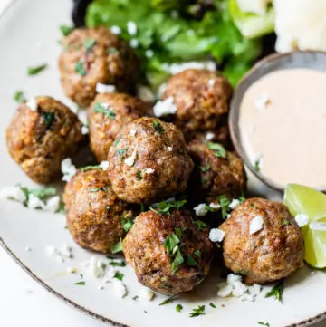 meatballs on a plate with side salad and sauce