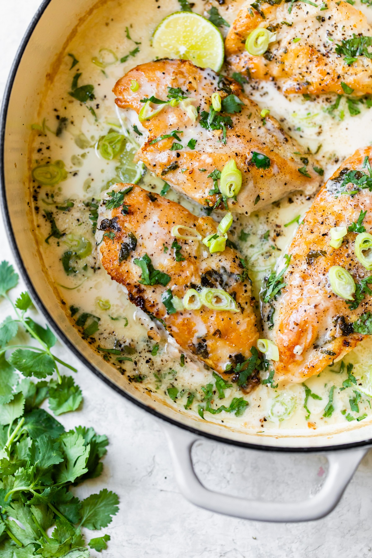 chicken in a skillet with sauce and lime wedges