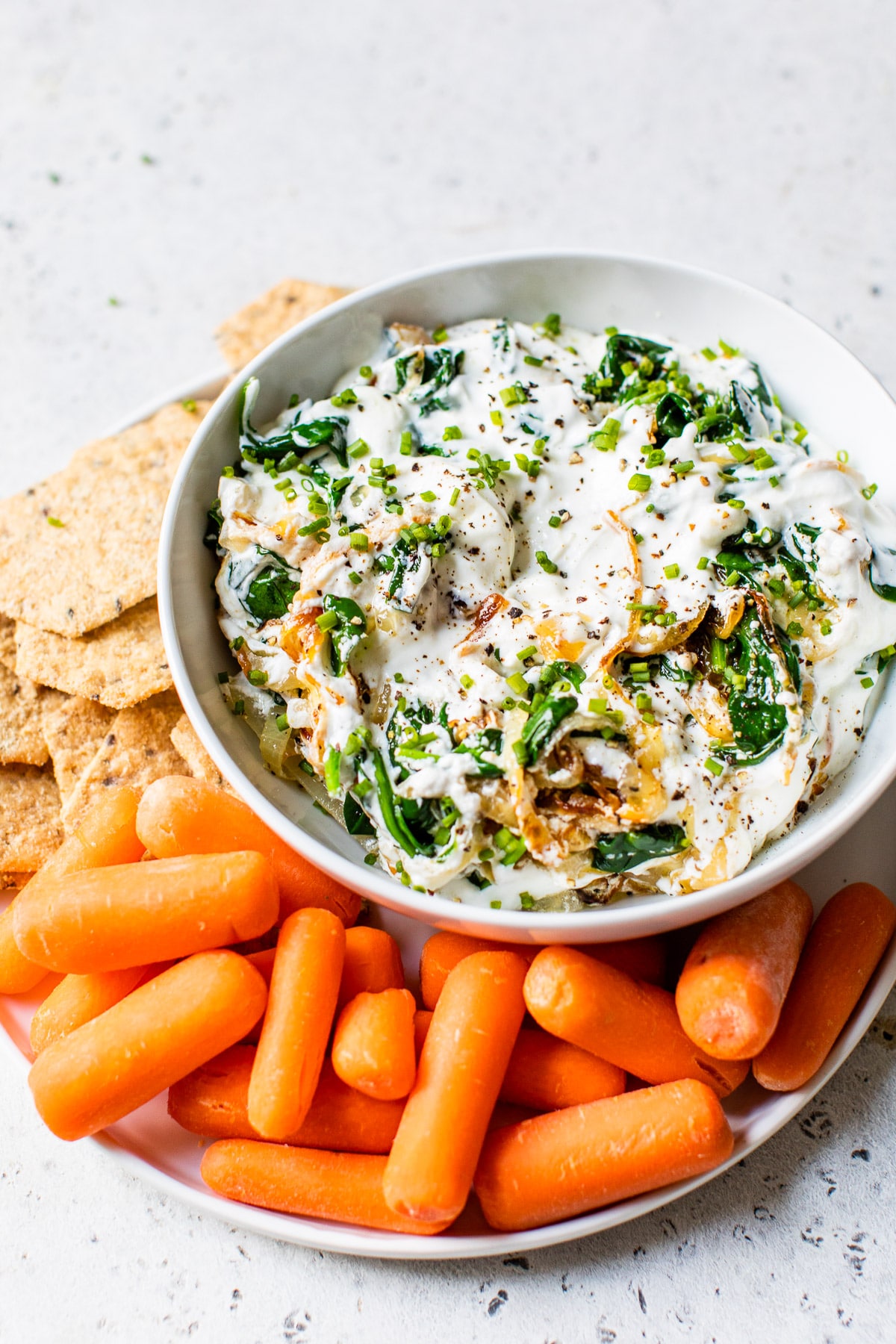 bowl with yogurt surrounded by baby carrots and crackers