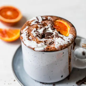 a glass of hot chocolate topped with whipped cream and an orange wedge