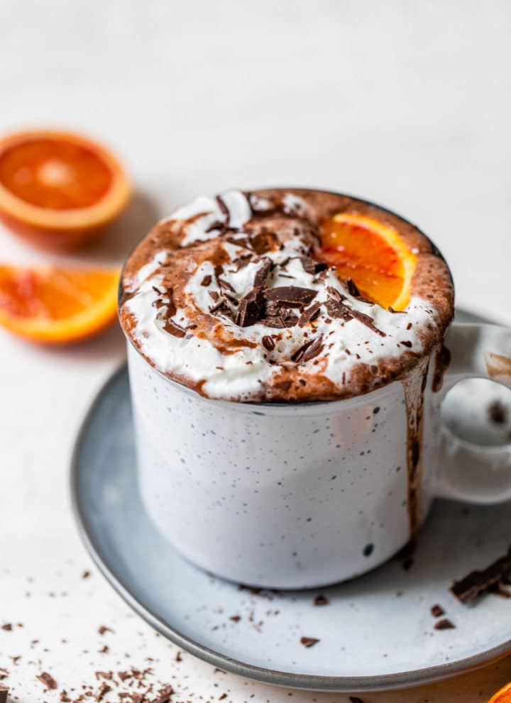 a glass of hot chocolate topped with whipped cream and an orange wedge