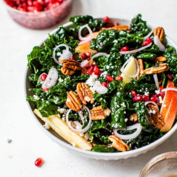 kale in a bowl with apple, pecans and pomegranate seeds