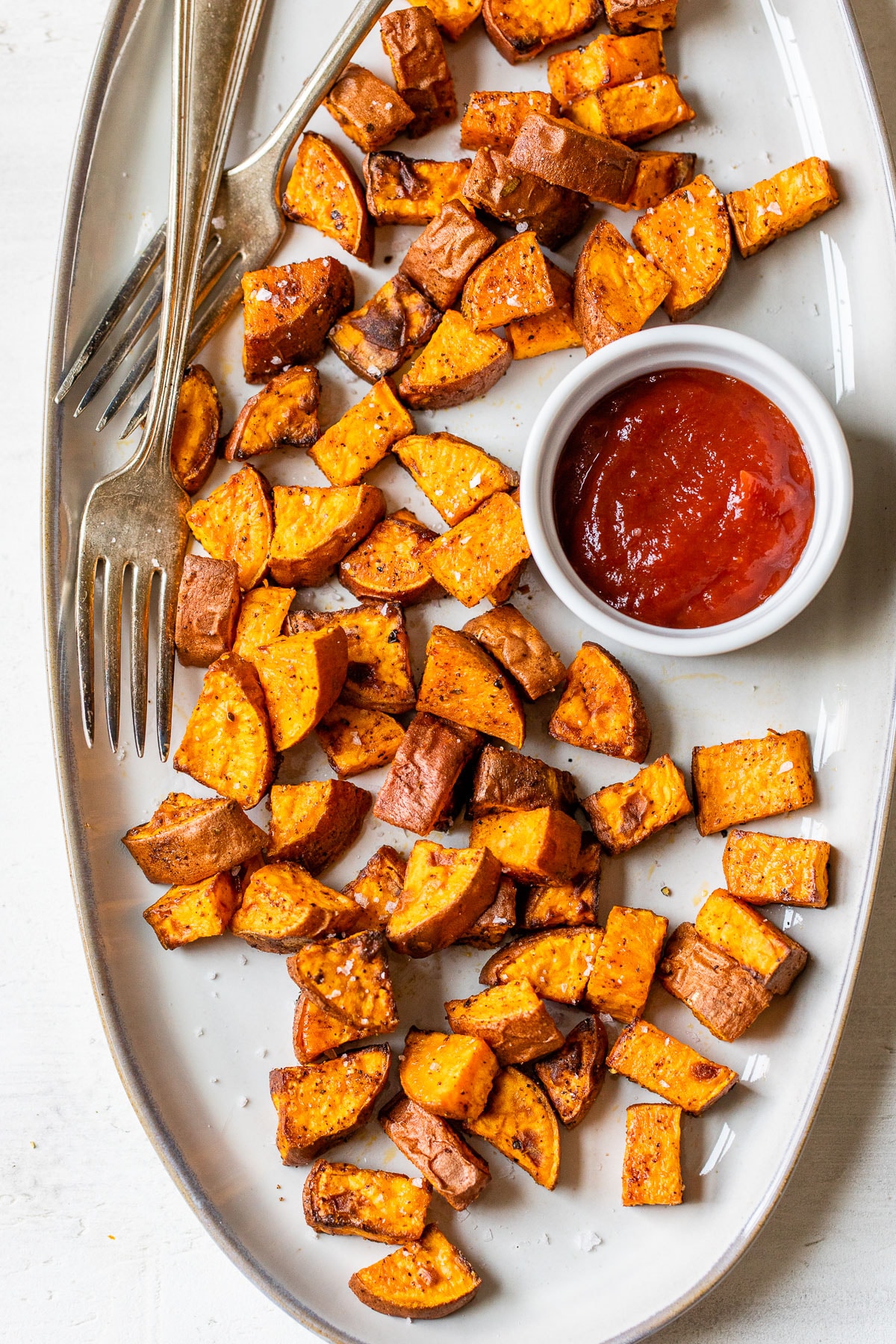 cooked sweet potatoes on a plate with a side of ketchup