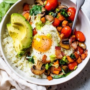bowl filled with cauliflower rice, vegetables, avocado, and a fried egg