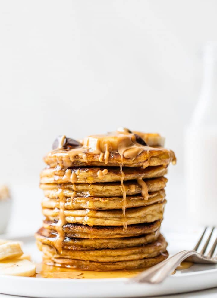 stack of pancakes on a plate with peanut butter and maple syrup