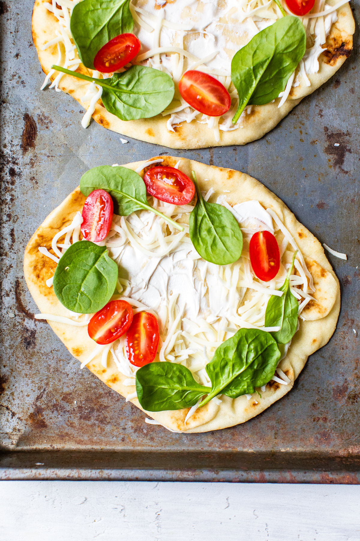 naan on a baking sheet with tomatoes and spinach