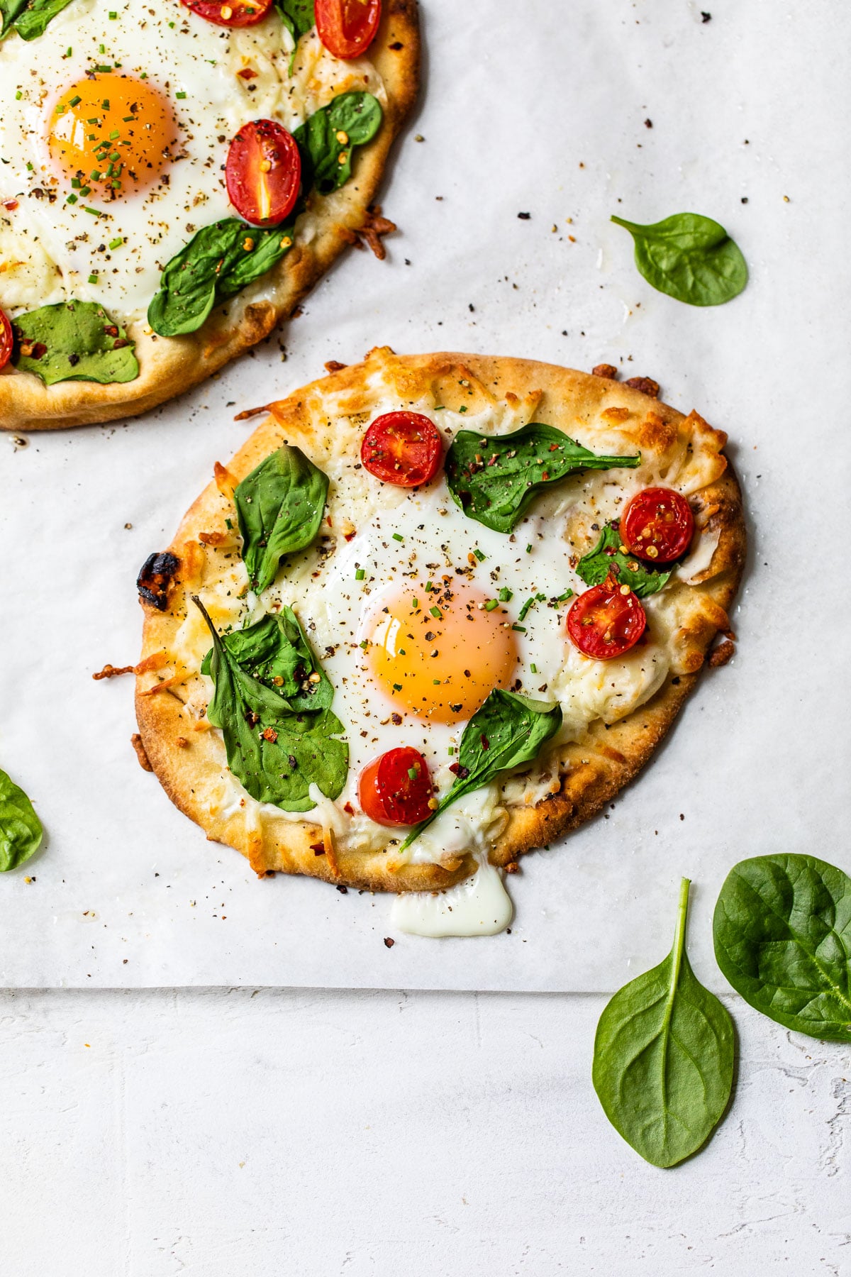 naan on parchment paper topped with vegetables, cheese and an egg