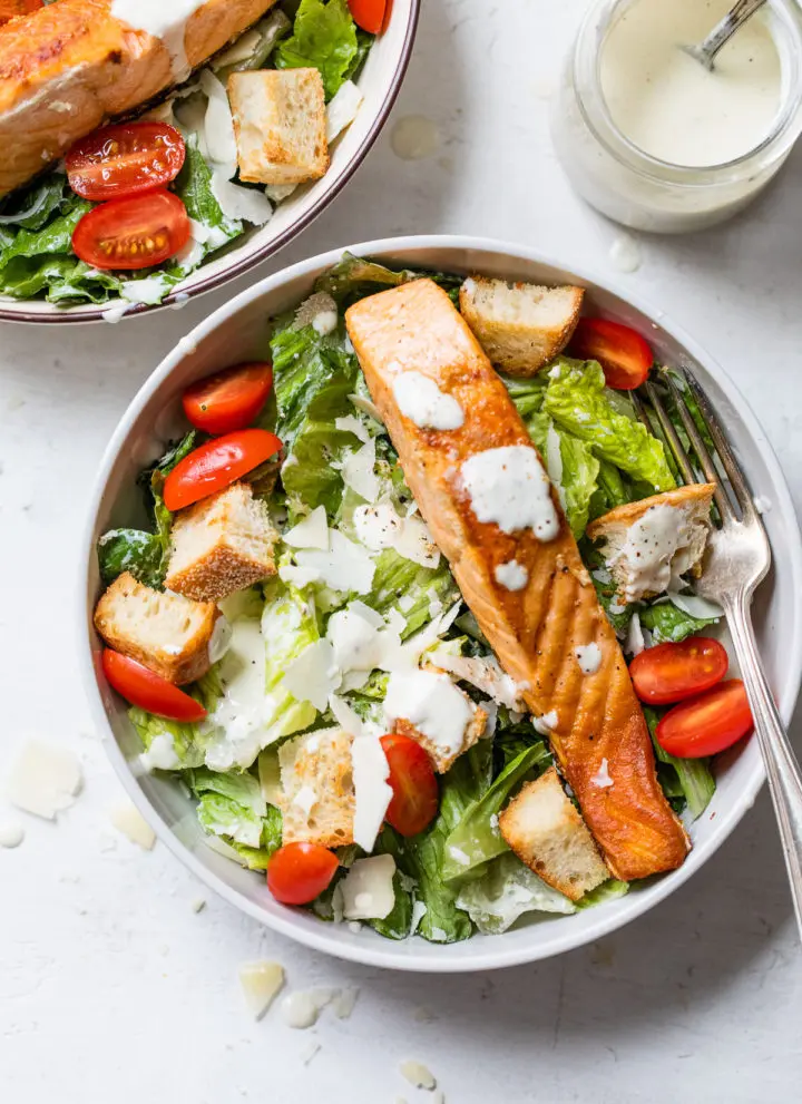 bowl of lettuce topped with grape tomatoes and cooked salmon