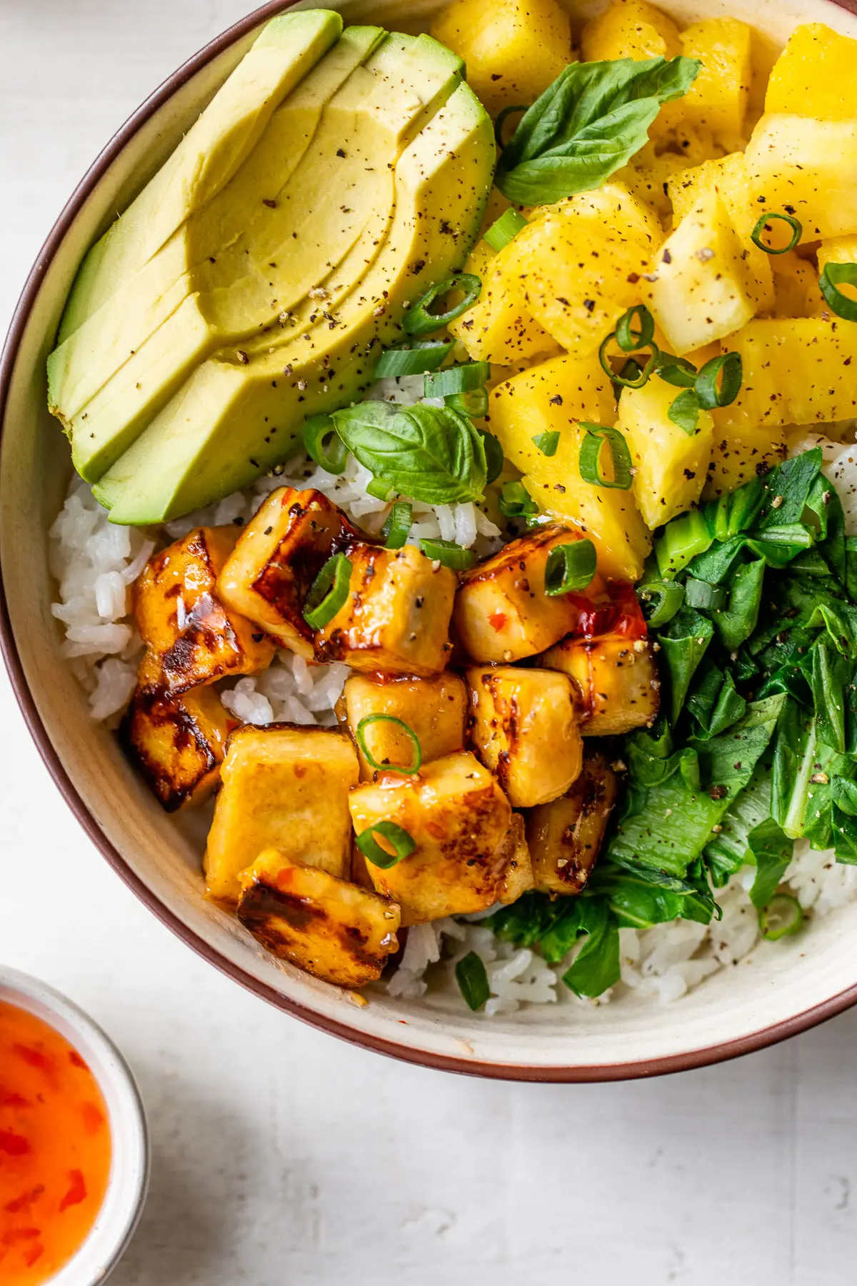 close up photo of crispy tofu in a bowl with rice and sliced avocado