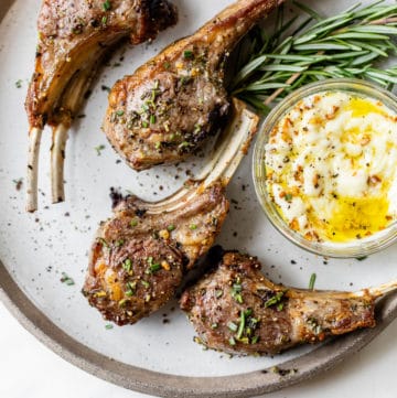 cooked lamb chops on a plate next to a small dish of aioli