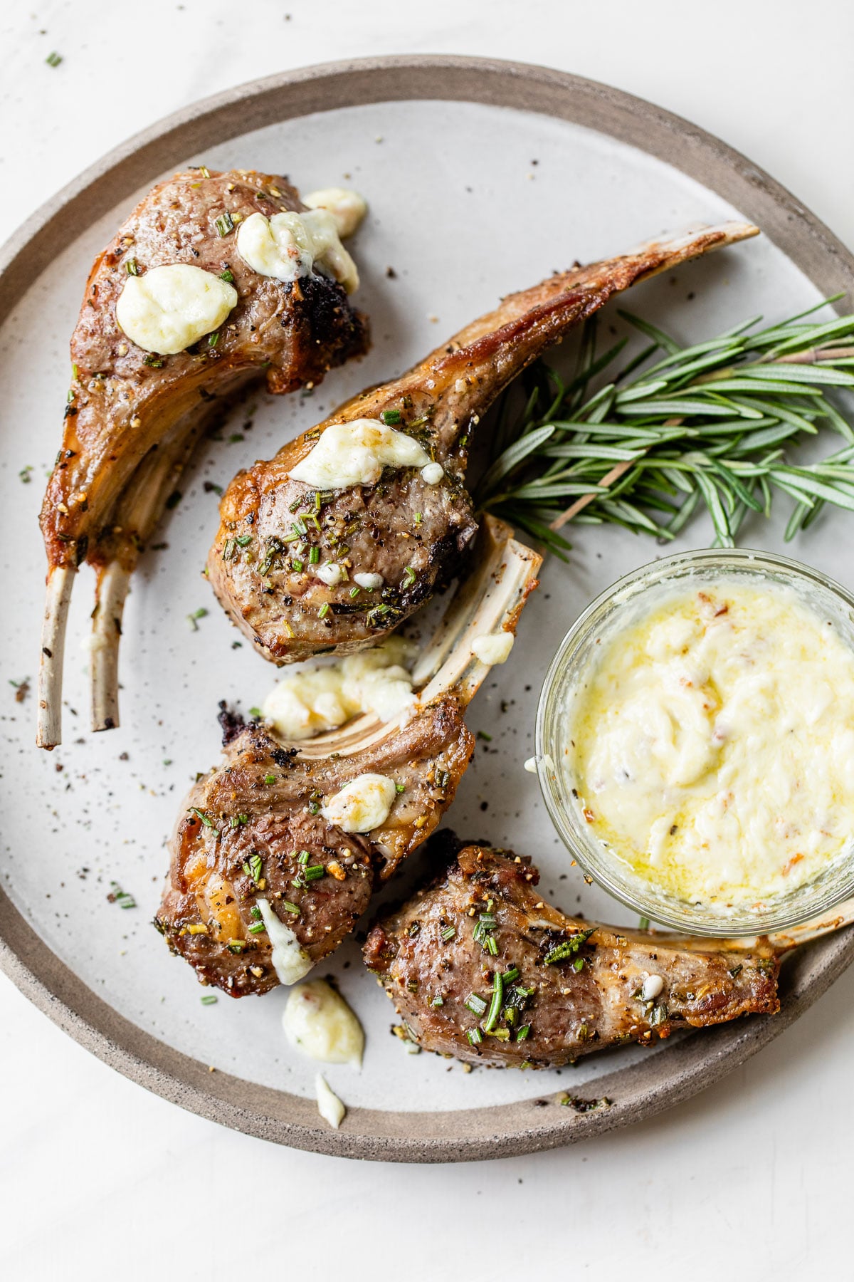 four lamb chops on a plate with aioli and fresh rosemary