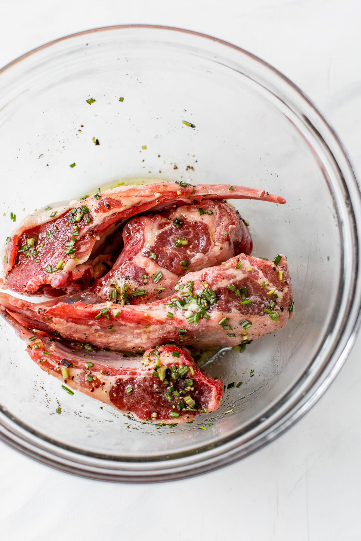 raw lamb chops marinating in a large glass bowl