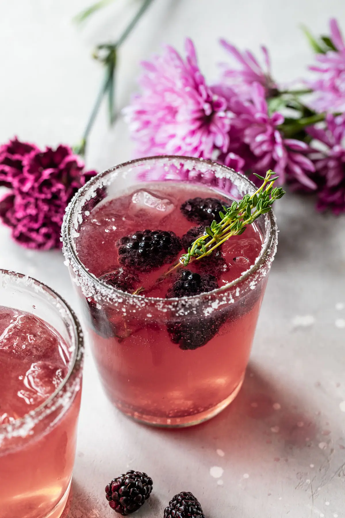 purple cocktail with blackberries and purple flowers in the background