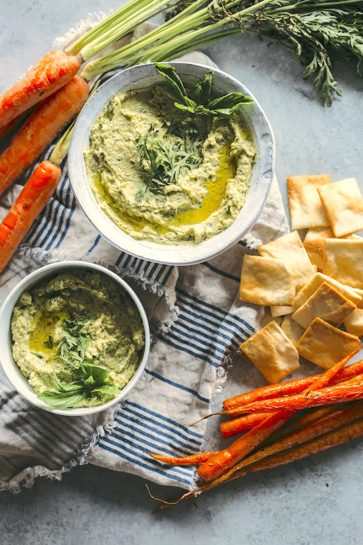 pesto hummus in a bowl on a table with carrots and pita chips
