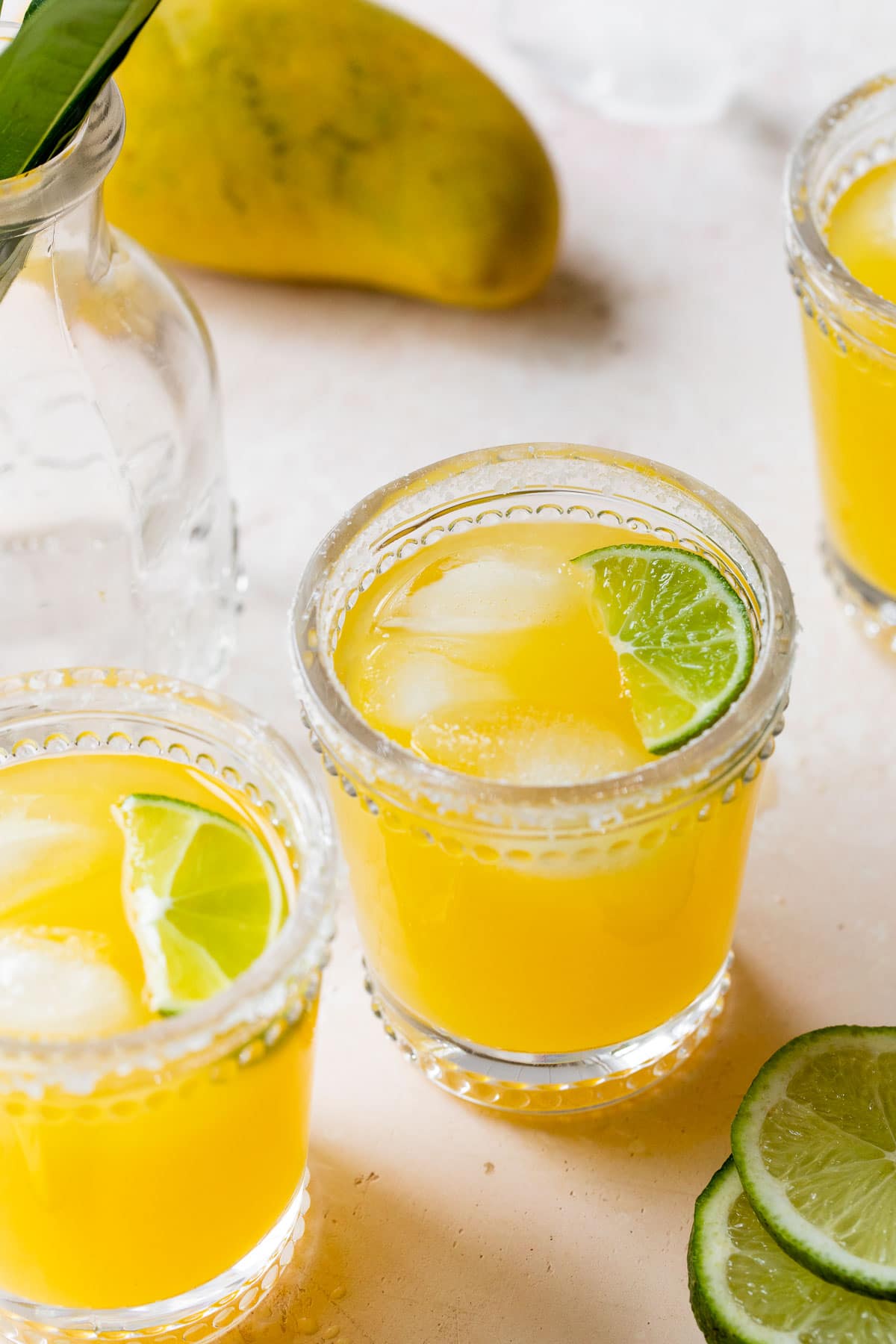 three glasses filled with mango juice and a lime wedge