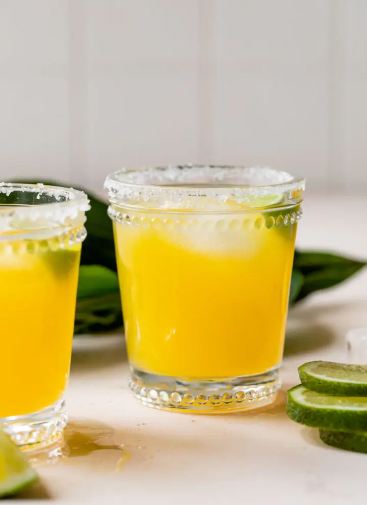 mango margarita in a glass with lime wedges