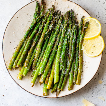 cooked asparagus on a plate with lemon wedges