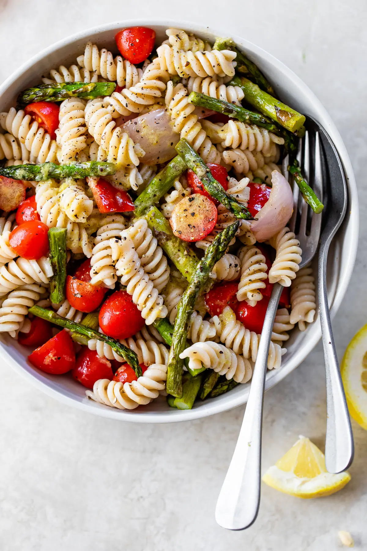 rotini pasta in a white bowl with chopped asparagus, tomatoes and red onion