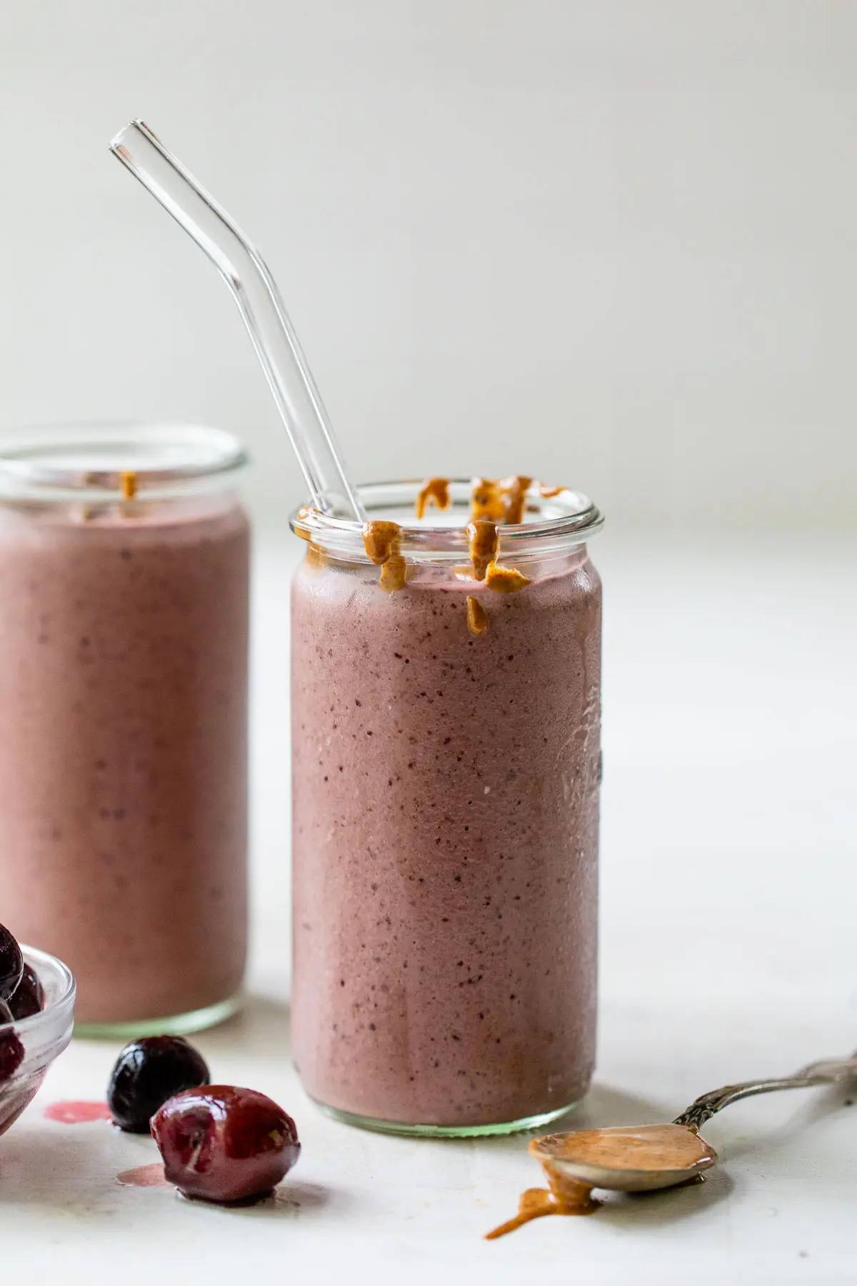 a clear glass with a red-colored smoothie beside a few frozen cherries