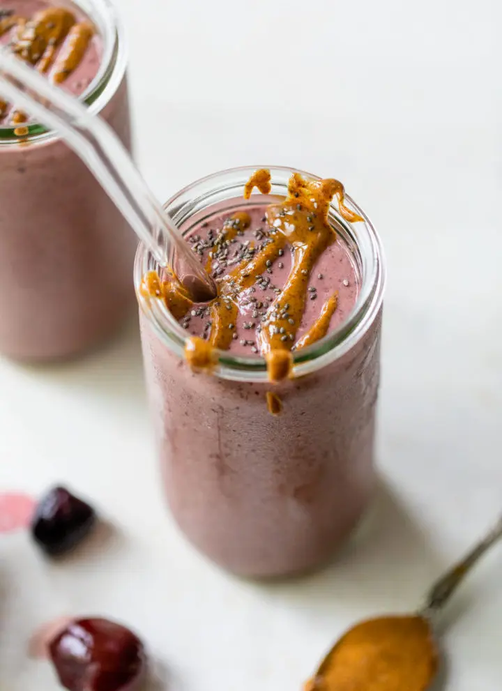 a cherry-colored smoothie in a tall glass drizzled with almond butter
