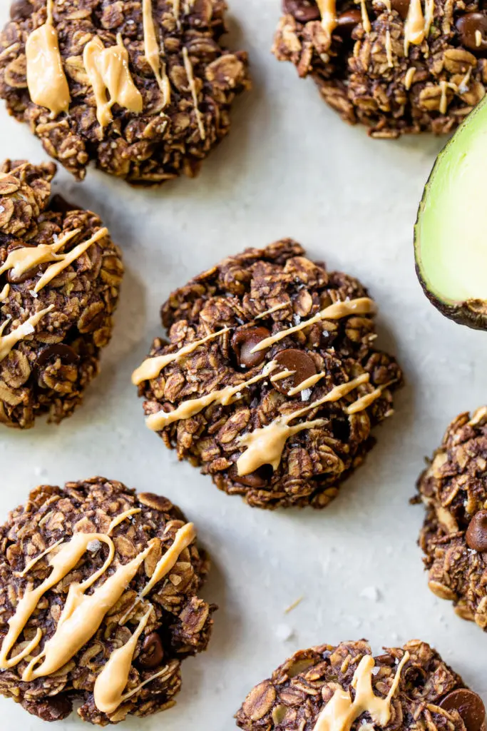 chocolate oatmeal cookies drizzled with peanut butter beside half of an avocado