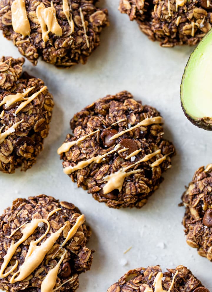 chocolate oatmeal cookies drizzled with peanut butter beside half of an avocado