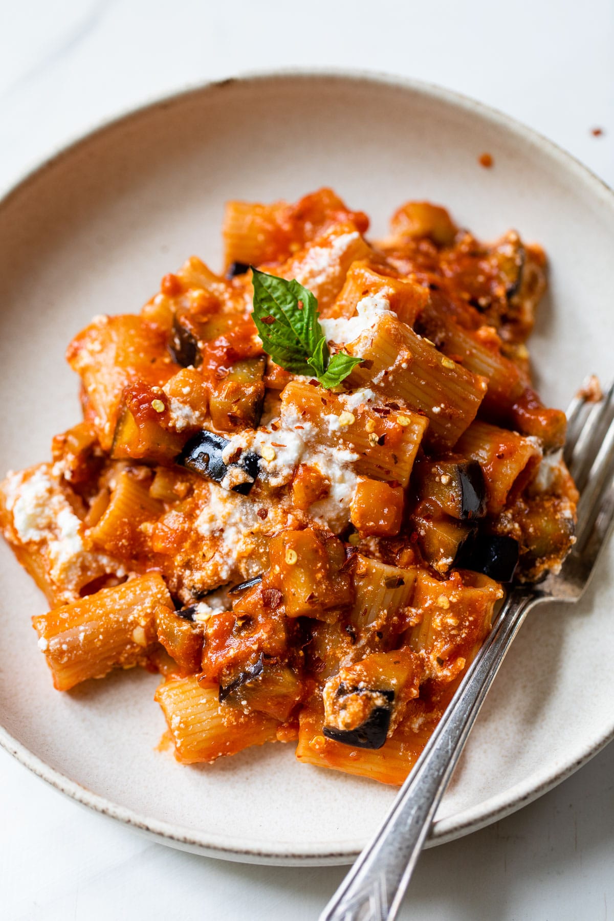 bowl filled with rigatoni pasta, cooked eggplant and topped with fresh basil
