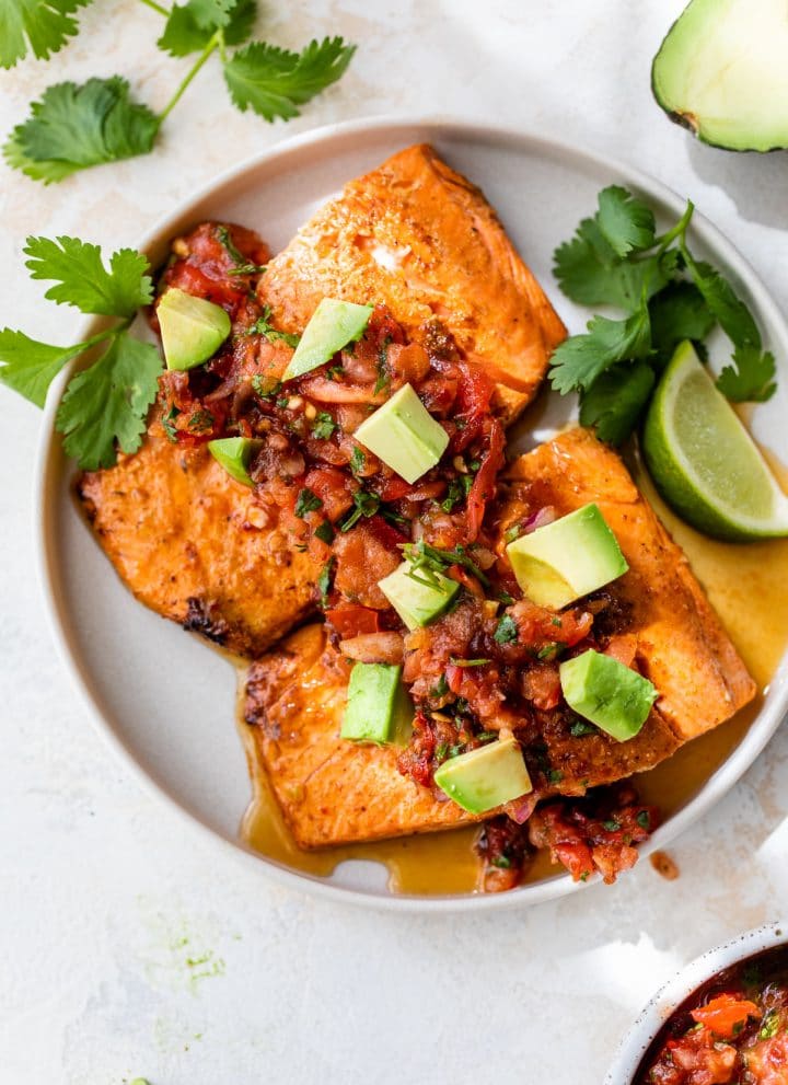 two salmon fillets on a plate topped with salsa and diced avocado