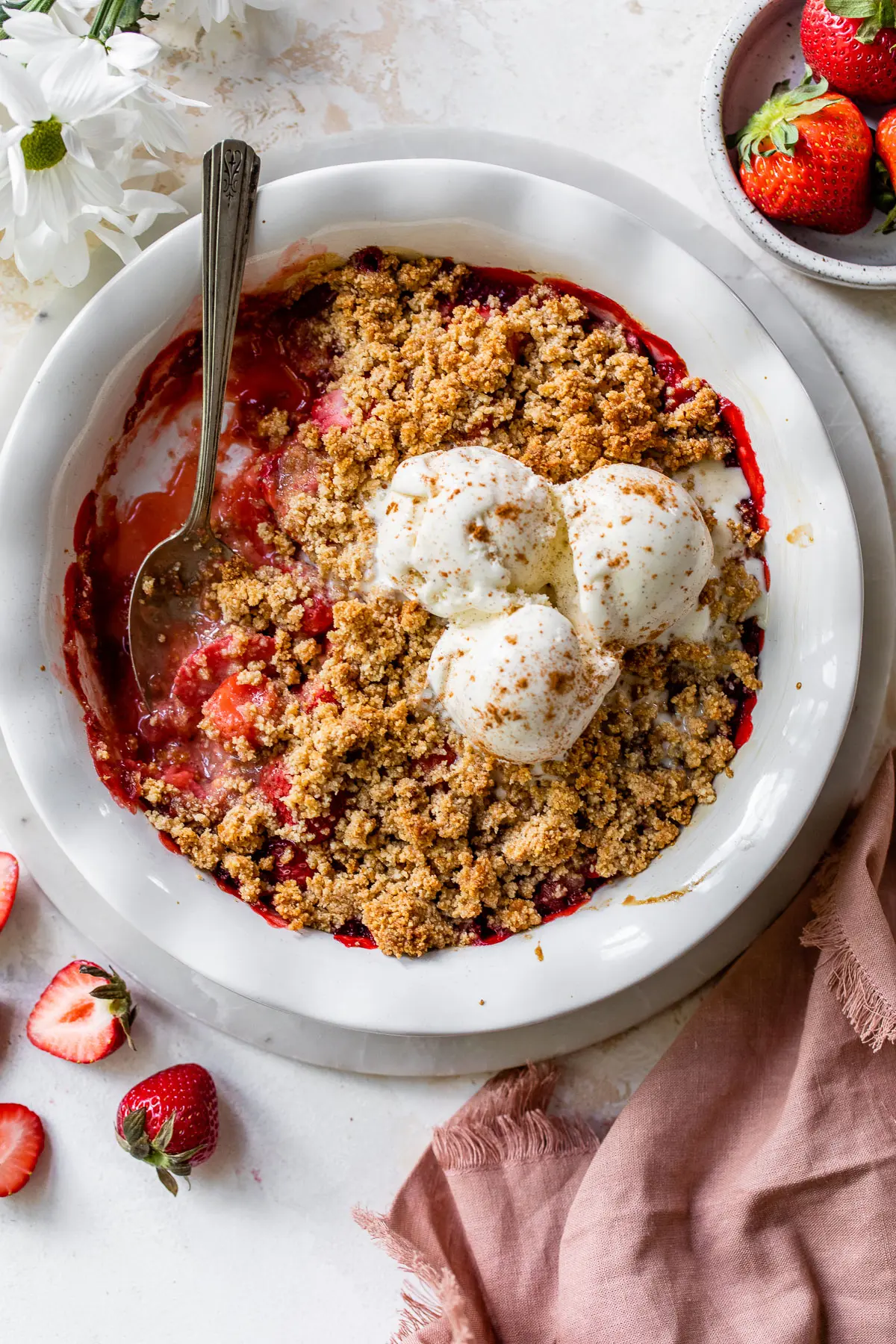 strawberry crisp in a white pie pan topped with three scoops of vanilla ice cream