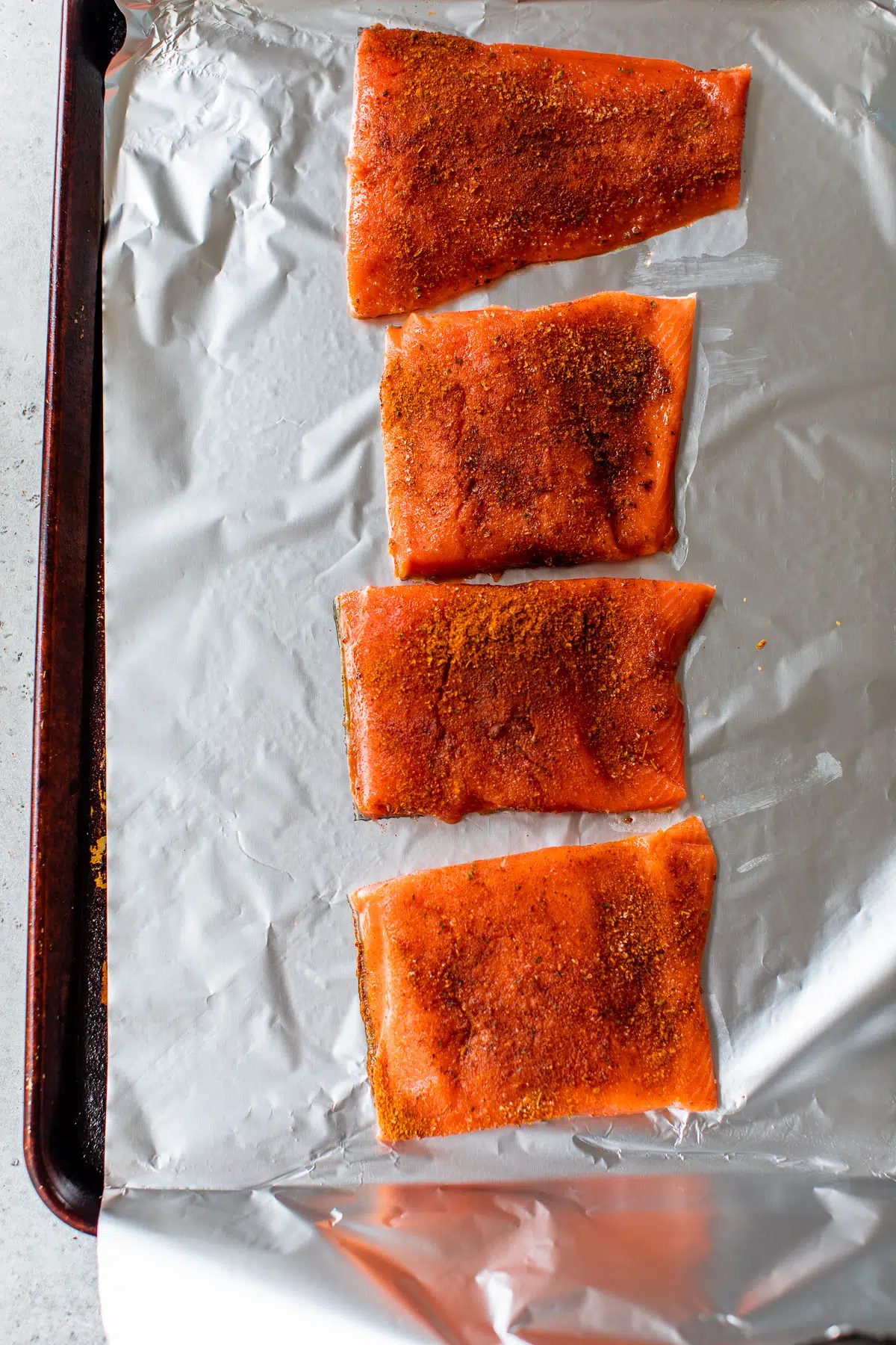 raw salmon fillets on a baking sheet sprinkled with cajun seasoning