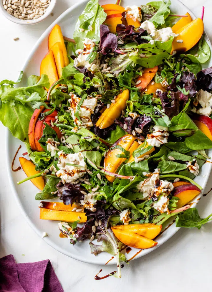mixed greens on a platter with sliced peaches and burrata cheese