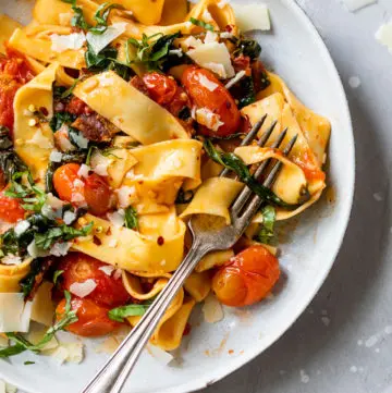 long cooked pasta in a bowl with grape tomatoes and chopped basil