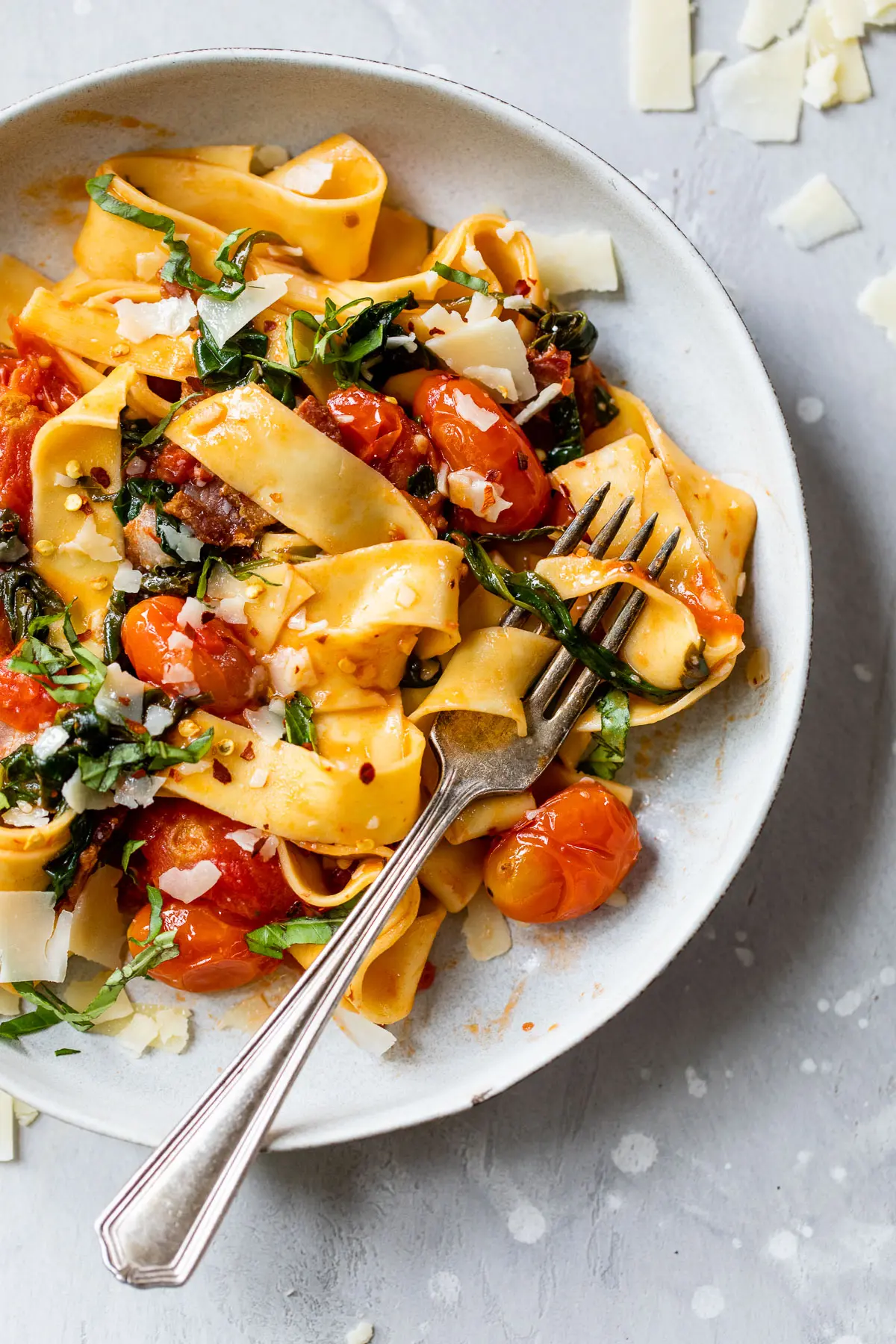 long cooked pasta in a bowl with grape tomatoes and chopped basil