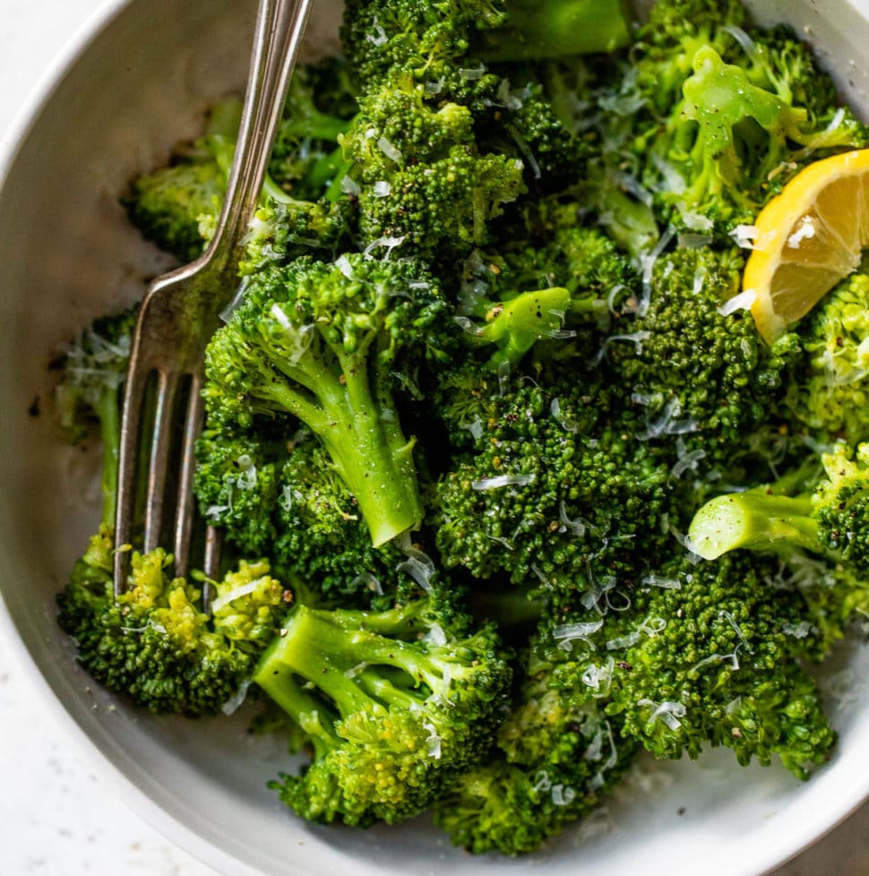 a large bowl of cooked broccoli sprinkled with grated cheese