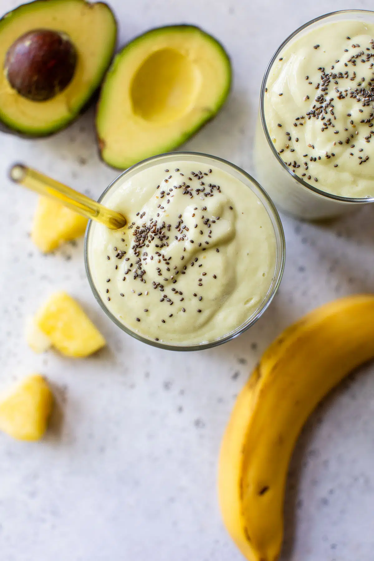 thick pineapple smoothie in a glass beside a banana and avocado