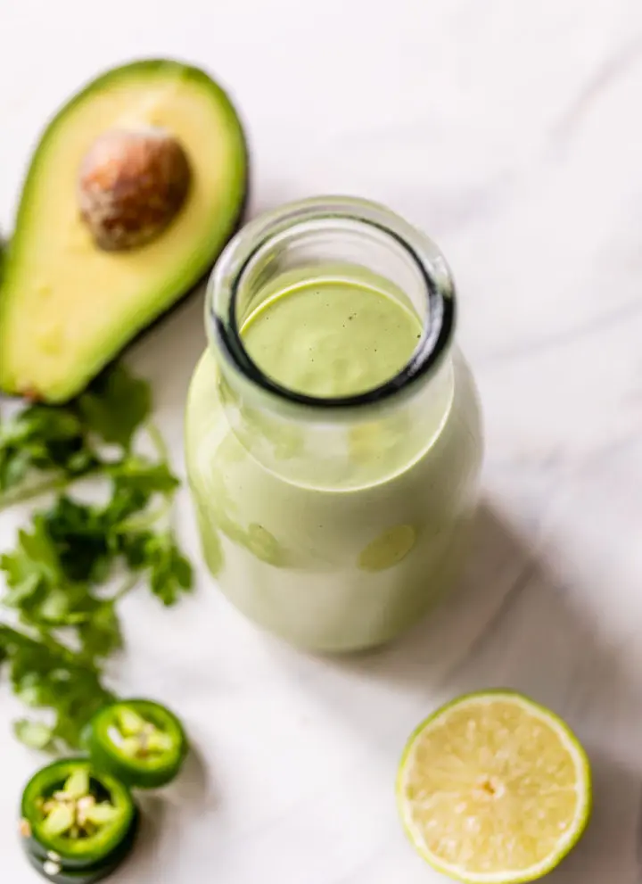 green dressing in a glass jar beside an avocado, lime and cilantro