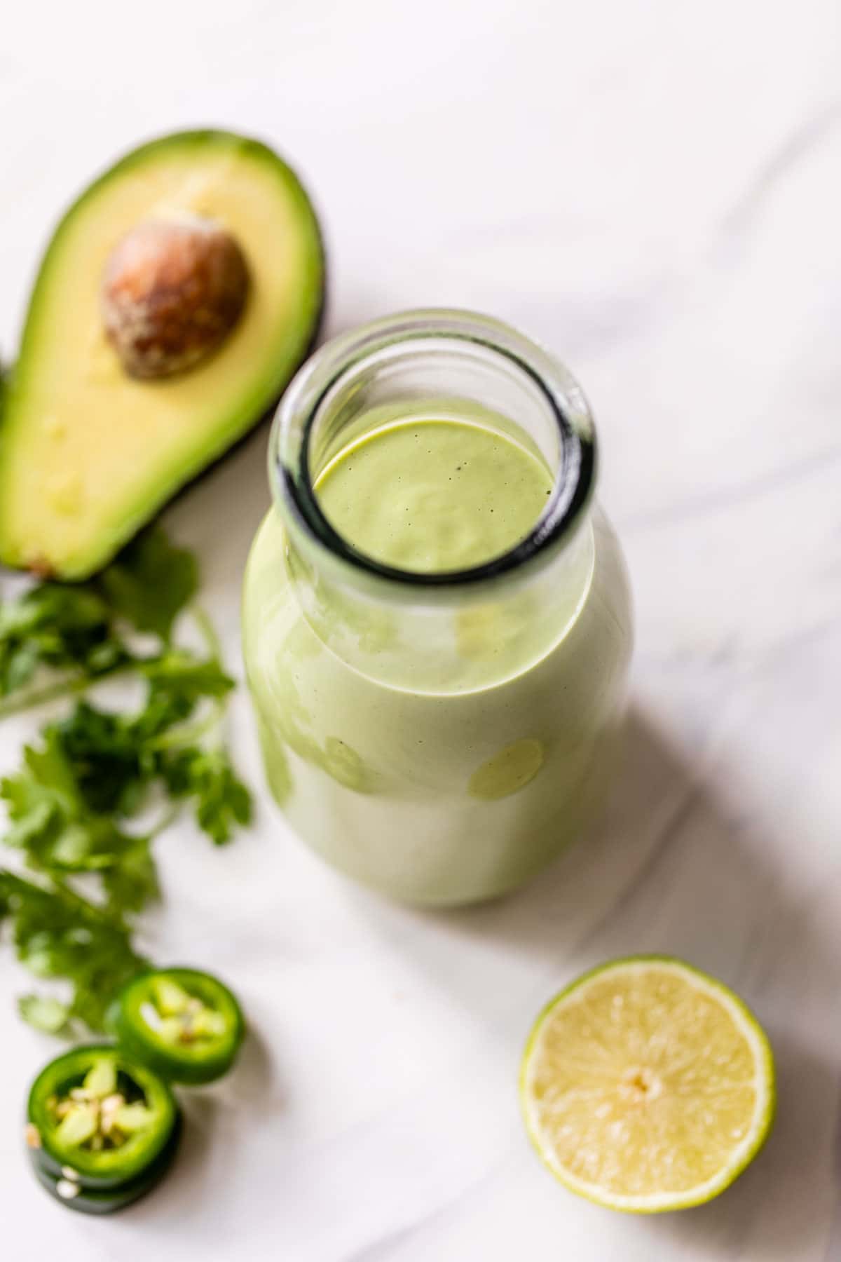 green dressing in a glass jar beside an avocado, lime and cilantro