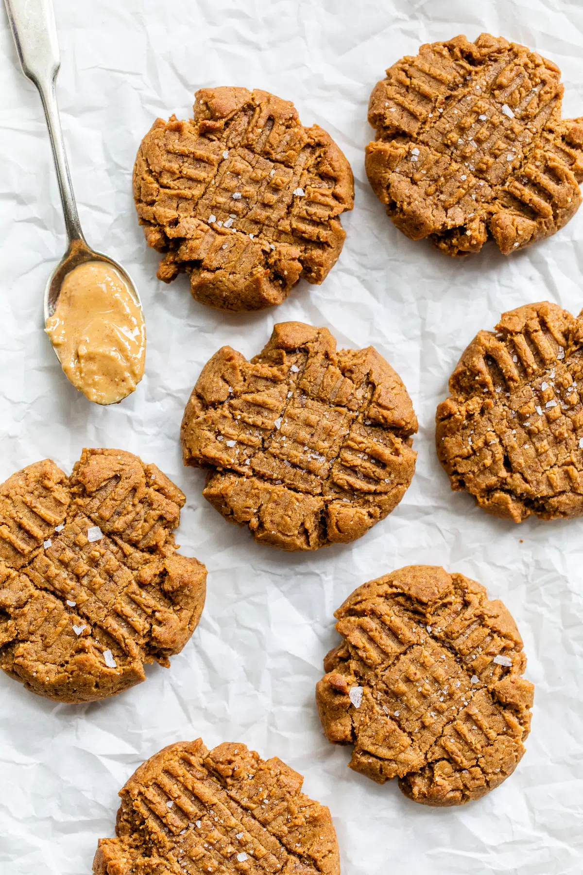 peanut butter cookies on parchment beside a spoon of peanut butter