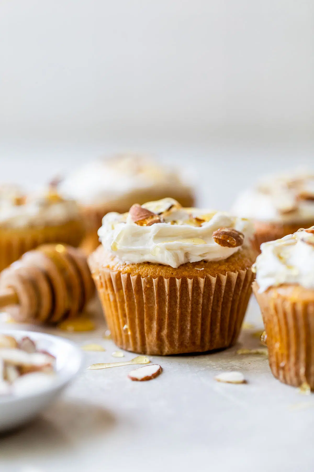 yellow cupcakes topped with white icing, sliced almonds and a drizzle of honey